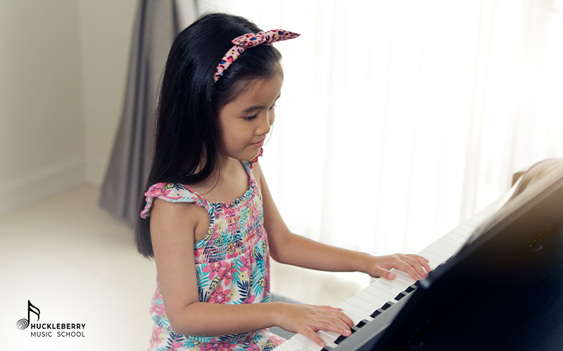 Young girl focused on playing piano keys in bright room.